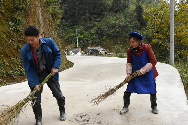 今年，周胜举的妻子担任村里的保洁员，图为他帮助妻子打扫村公路的卫生。