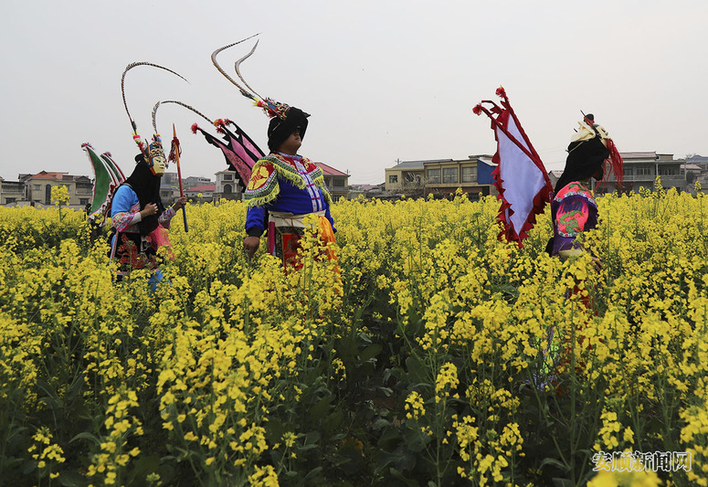 3月17日，地戏表演队员走在贵州省安顺市西秀区狗场屯村的油菜花地里。